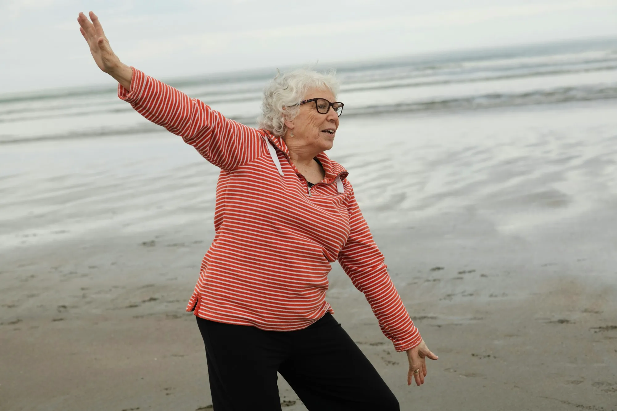Una mujer mayor practica tai chi en la playa